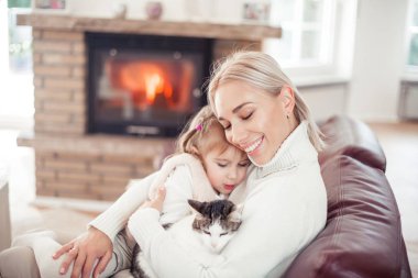 Güzel anne, küçük kızı ve bir kedi şömine yakın kanepede oturuyor. Aile ev iç. Rahat.