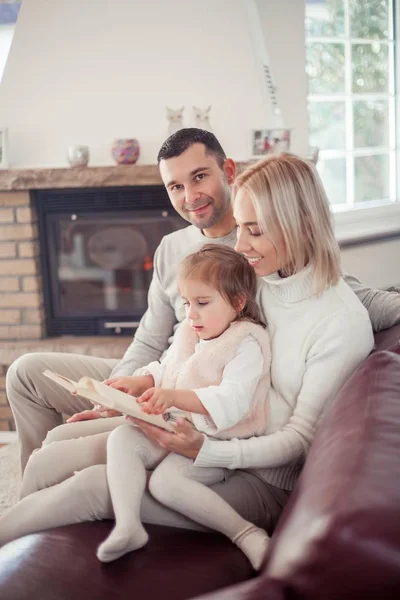 Vacker ung familj läser en bok vid den öppna spisen. Cozy. — Stockfoto