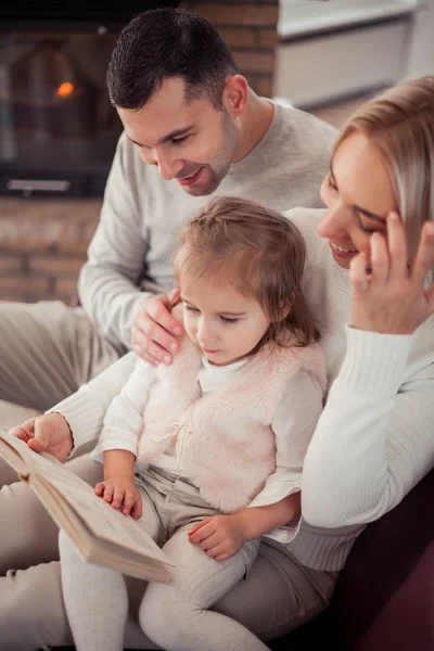 Vacker ung familj läser en bok vid den öppna spisen. Cozy. — Stockfoto