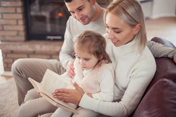 Mooie jonge gezin is het lezen van een boek bij de open haard. Gezellige. — Stockfoto