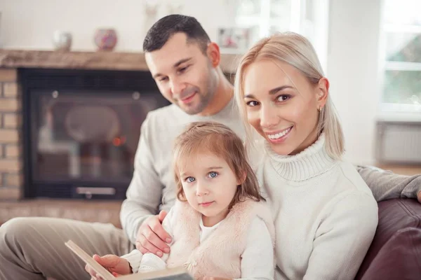 Vacker ung familj läser en bok vid den öppna spisen. Cozy. — Stockfoto