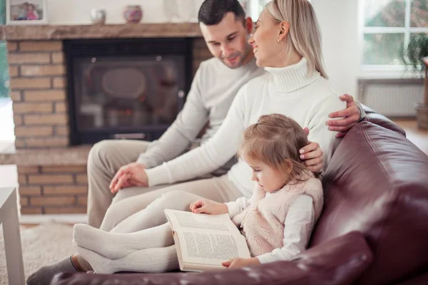 Mooie jonge gezin is het lezen van een boek bij de open haard. Gezellige. — Stockfoto