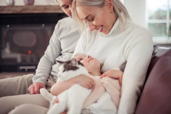 De familie zit op de Bank bij de open haard. Moeder, vader, dochter en kat in het interieur. Gezellige. — Stockfoto