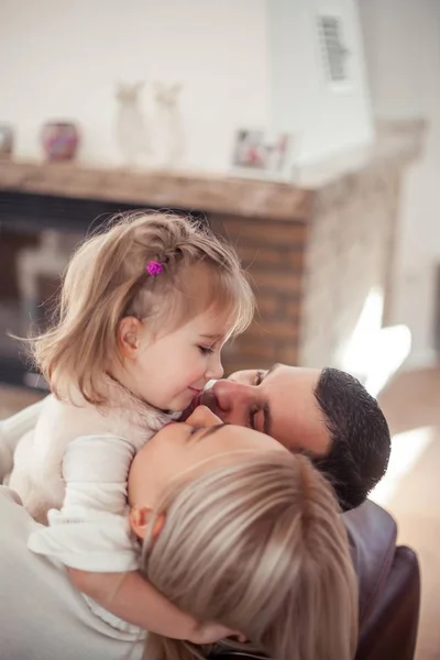 De familie zit op de Bank bij de open haard. Moeder, vader, dochter in het interieur. Gezellige. — Stockfoto