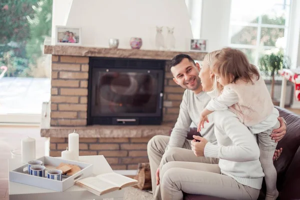 De familie zit op de Bank bij de open haard. Moeder, vader, dochter in het interieur. Gezellige. — Stockfoto