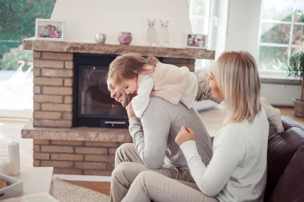 A família se senta no sofá perto da lareira. Mãe, pai, filha no interior da casa. Aconchegante . — Fotografia de Stock