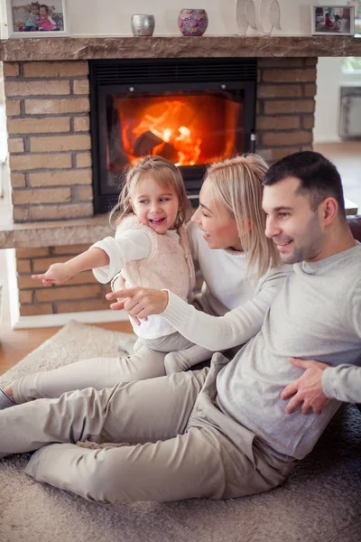 De familie zit op de Bank bij de open haard. Moeder, vader, dochter in het interieur. Gezellige. — Stockfoto