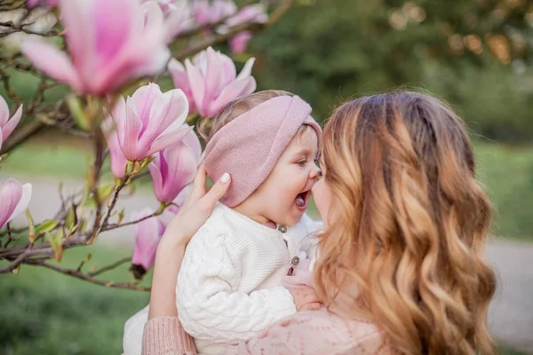 Schöne junge Mutter und kleine Tochter in der Nähe der Magnolie. Familienporträt im Frühling. — Stockfoto