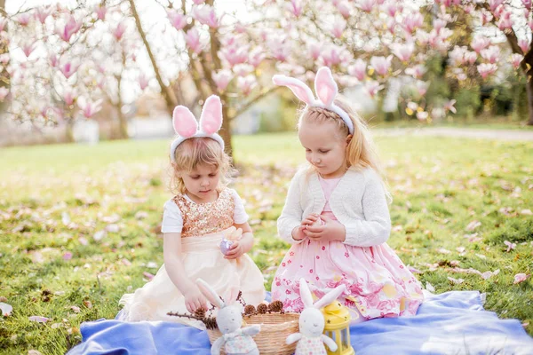 Little cute girls are sitting on the grass near the mogolia. Girls in costumes Easter bunnies. — Stock Photo, Image