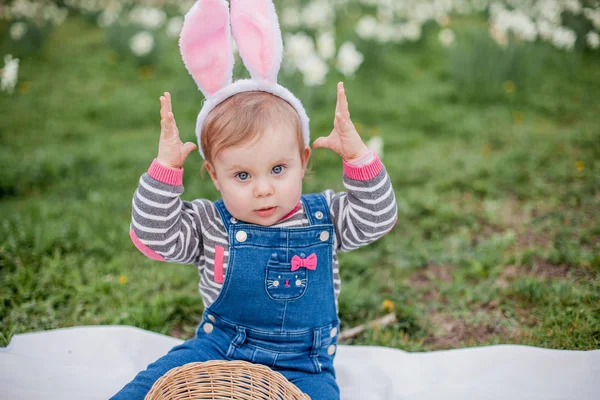 Liten söt flicka som sitter på gräset nära påsk liljor. Flicka i kostym av påsk haren. — Stockfoto