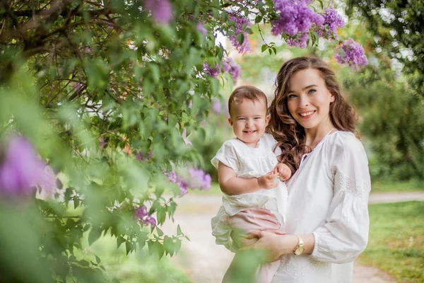 Gyönyörű fiatal anya és a kis aranyos lánya boldog közelében lila. Portré az anya és lánya. Tavaszi. — Stock Fotó