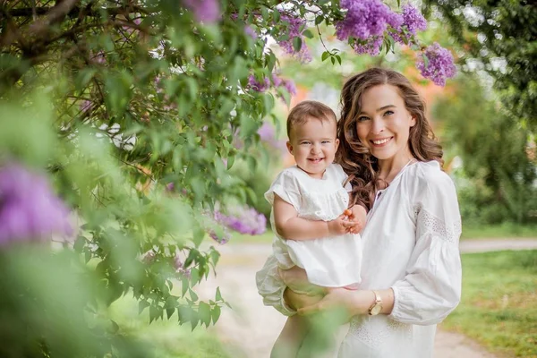 Beautiful young mother and little cute daughter are happy near the lilac. Portrait of mom and daughter. Spring. — Stock Photo, Image