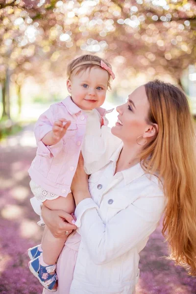 Gyönyörű fiatal anya és a kis aranyos lánya boldog séta egy virágos parkban. Portré az anya és lánya. Cseresznye virágok. — Stock Fotó