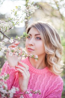 Çiçekli bir ağacın yanında genç bir sarışının bahar portresi. Mutlu genç kadın.