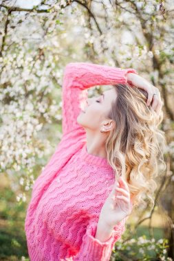 Çiçekli bir ağacın yanında genç bir sarışının bahar portresi. Mutlu genç kadın.