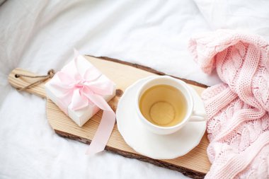 Beyaz kupa çay, hediye kutusu ile yatağın üstüne kurdele ile. Yatakta kahvaltı. Rahat. Pembe kareli. Pamuk.