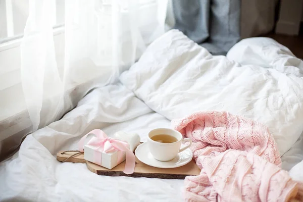 Taza blanca con té, caja de regalo con cinta en la cama. Desayuno en la cama. Acogedor. Plaid rosa. Algodón . — Foto de Stock