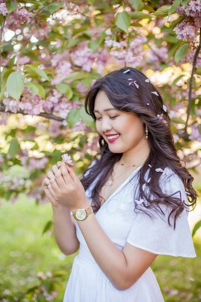 Mladá krásná asijská žena v bílých šatech prochází v květém parku. Sakura. Kvetoucí stromy. — Stock fotografie