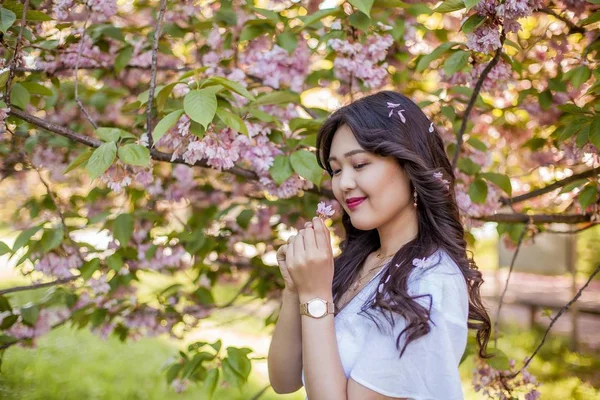 Mladá krásná asijská žena v bílých šatech prochází v květém parku. Sakura. Kvetoucí stromy. — Stock fotografie