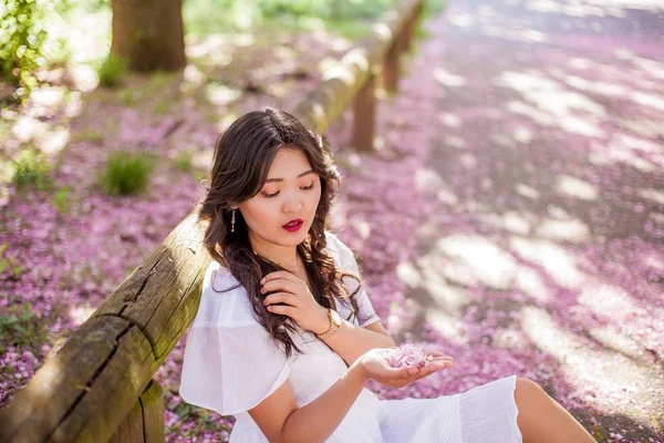 Mladá krásná asijská žena v bílých šatech prochází v květém parku. Sakura. Kvetoucí stromy. — Stock fotografie