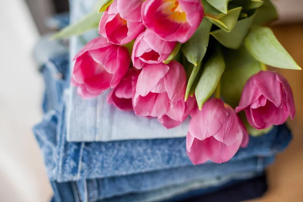 Ein Strauß Tulpen liegt auf einem Haufen Jeans. Kleidung. — Stockfoto