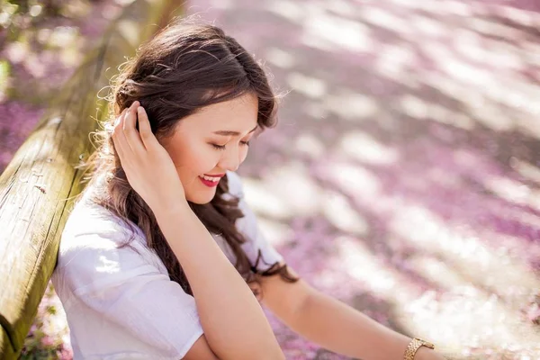 Uma jovem mulher asiática bonita em um vestido branco caminha em um parque florido. Sakura. Plantas em flor . — Fotografia de Stock