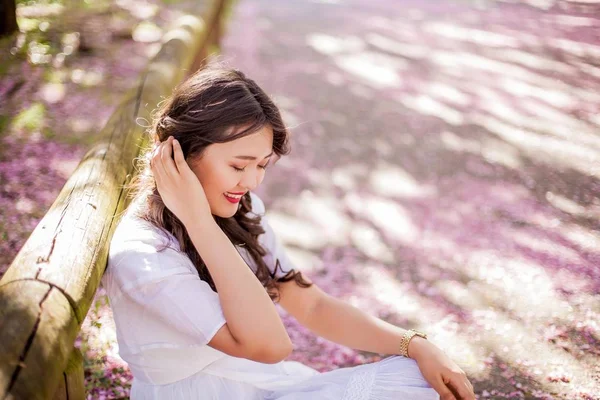 Uma jovem mulher asiática bonita em um vestido branco caminha em um parque florido. Sakura. Plantas em flor . — Fotografia de Stock