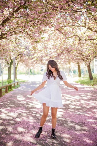 Mladá krásná asijská žena v bílých šatech prochází v květém parku. Sakura. Kvetoucí stromy. — Stock fotografie