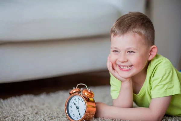 Menino bonito de 4 anos está no tapete e perto do despertador. Bom dia. Despertar . — Fotografia de Stock