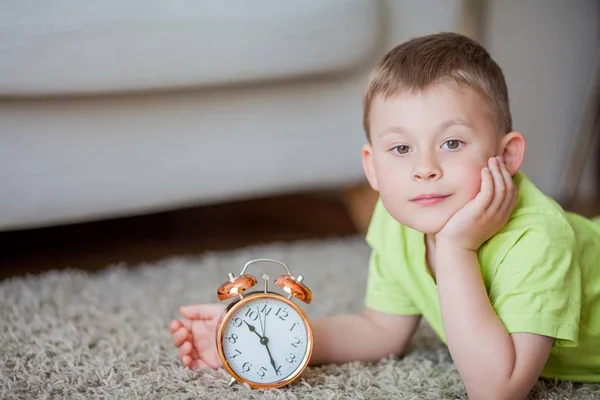 Menino bonito de 4 anos está no tapete e perto do despertador. Bom dia. Despertar . — Fotografia de Stock