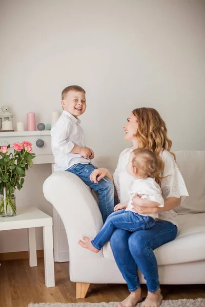 Mooie jonge moeder, kleine zoon, kleine dochter zitten op de Bank thuis. Moederdag. Een gelukkige familie. Gezellige. — Stockfoto