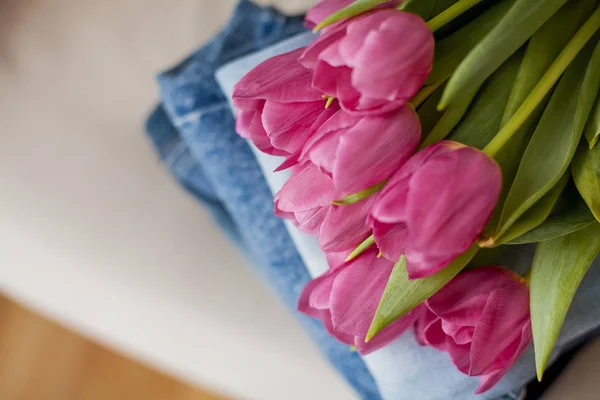 Nahaufnahme. Ein Strauß Tulpen liegt auf einem Haufen Jeans. Kleidung. — Stockfoto