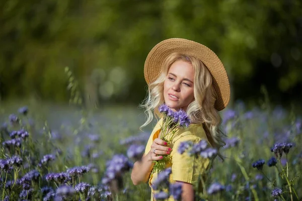 Mulher bonita jovem loira em um chapéu caminha através de um campo de flores roxas. Verão . — Fotografia de Stock