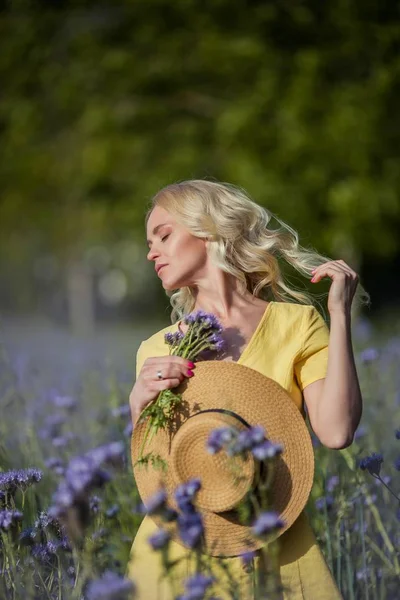 Jeune belle femme blonde dans un chapeau marche à travers un champ de fleurs violettes. Été . — Photo