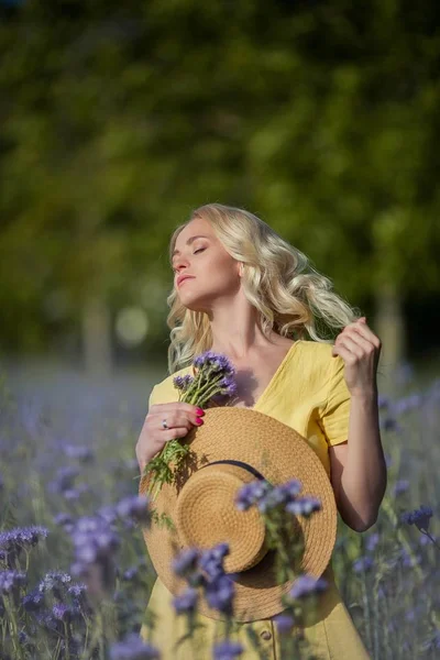 Jeune belle femme blonde dans un chapeau marche à travers un champ de fleurs violettes. Été . — Photo
