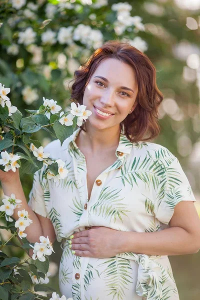 Beautiful young happy pregnant woman is standing near the blossoming tree. Motherhood. Love. Spring. — Stock Photo, Image