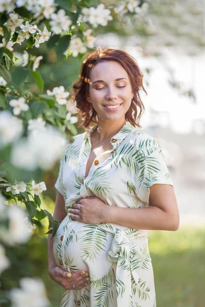 Wanita muda cantik yang bahagia sedang berdiri di dekat pohon yang sedang bermekaran. Keibuan. Cinta. Spring . — Stok Foto