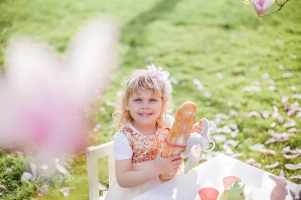 Dos niñas rubias lindas de 3 años están jugando en el parque cerca de una magnolia floreciente. Beber té. Semana Santa . —  Fotos de Stock