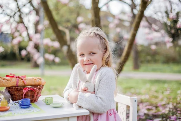 Dos niñas rubias lindas de 3 años están jugando en el parque cerca de una magnolia floreciente. Beber té. Semana Santa . —  Fotos de Stock