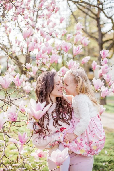 Beautiful young mother and little daughter near a blooming magnolia. Spring. Pink blooms. — Stock Photo, Image