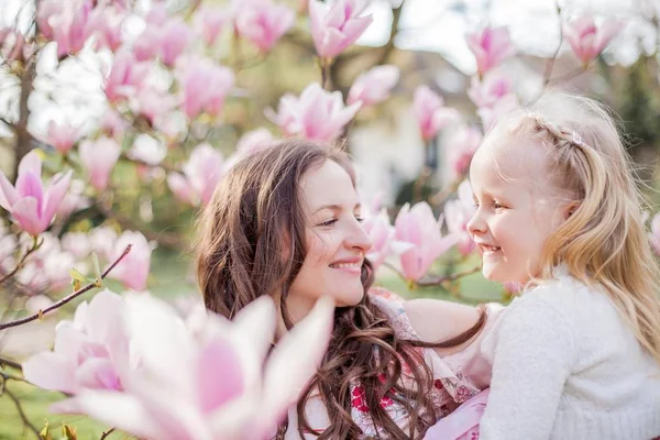 Bela jovem mãe e filhinha perto de uma magnólia florescente. Primavera. Flores cor de rosa . — Fotografia de Stock