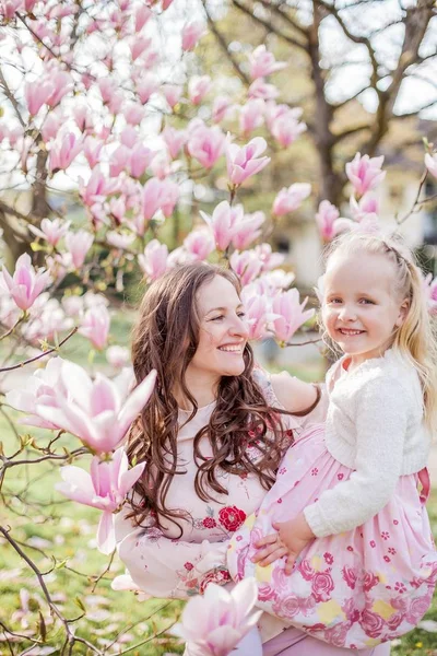Hermosa joven madre e hija pequeña cerca de una magnolia floreciente. Primavera. Floraciones rosadas . —  Fotos de Stock