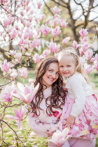 Gyönyörű fiatal anya és a kis lánya közelében virágzó magnólia. Tavaszi. Rózsaszín virágzik. — Stock Fotó