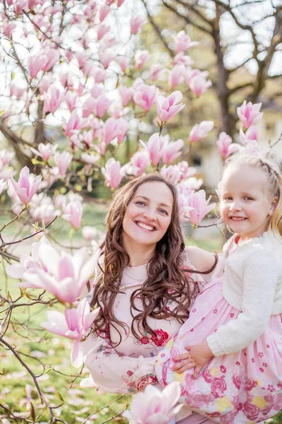 Beautiful young mother and little daughter near a blooming magnolia. Spring. Pink blooms. — Stock Photo, Image