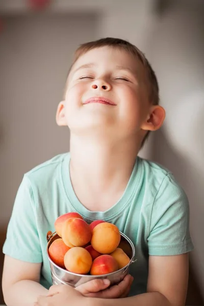 A little cute boy of 4 years old is eating juicy apricots from a bucket.