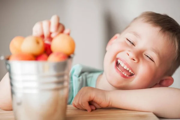 Un petit garçon mignon de 4 ans mange des abricots juteux d'un seau . — Photo