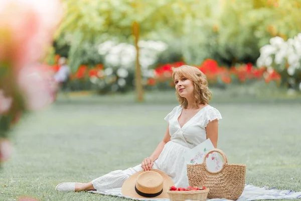 Jovem mulher grávida bonita em vestido branco está sentado no prado e comer morangos. Piquenique. Maternidade . — Fotografia de Stock