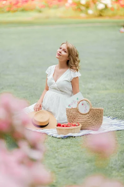 Beyaz elbiseli genç güzel hamile kadın çayırda oturuyor ve çilek yiyor. Piknik. Annelik. — Stok fotoğraf