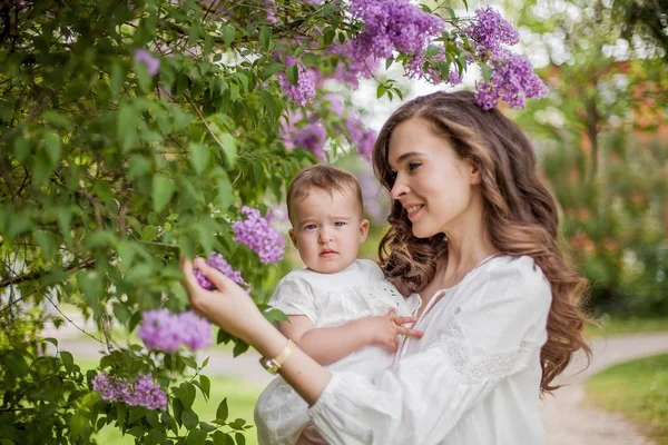 Прекрасные молодая мать и дочь рядом с цветущей сиренью. Весна . — стоковое фото