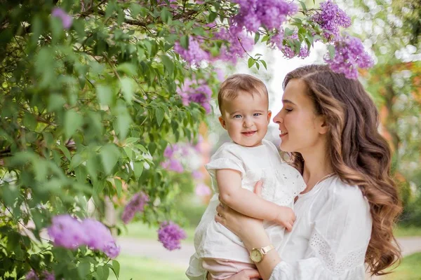 Piękna młoda matka i córka w pobliżu kwitnących bzu. Wiosna. — Zdjęcie stockowe